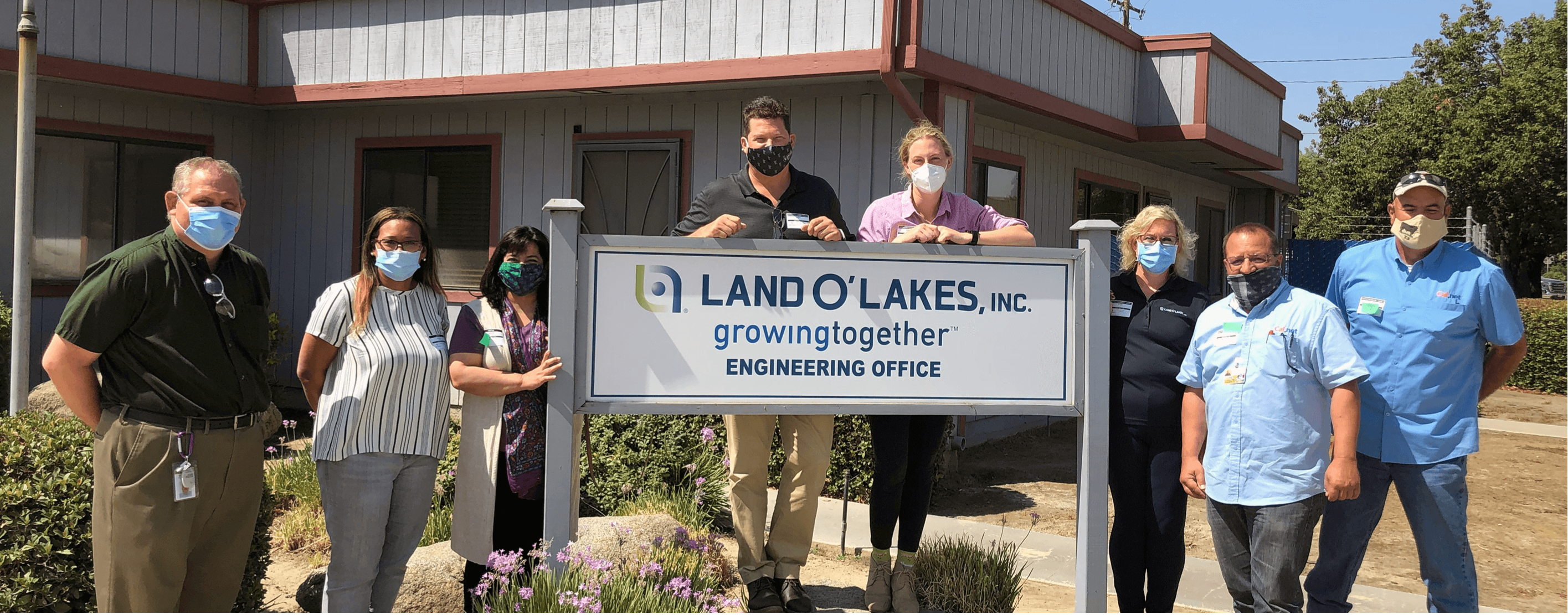 A group of Land O'Lakes employees standing next to a sign that says "Land O'Lakes, Inc. growing together engineering office ."