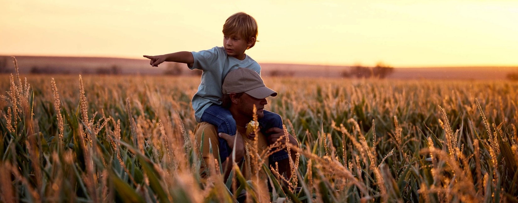 A man is standing in the field with a boy on his shoulders.