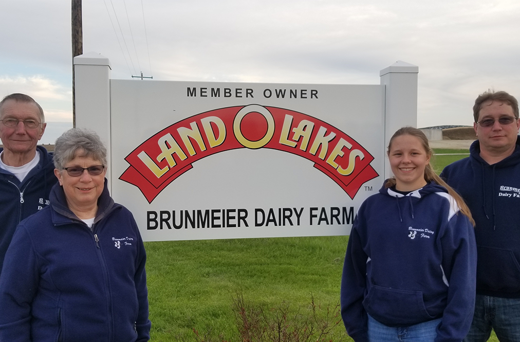 A Land O'Lakes Member Family Standing In Front Of A Land O'Lakes Sign