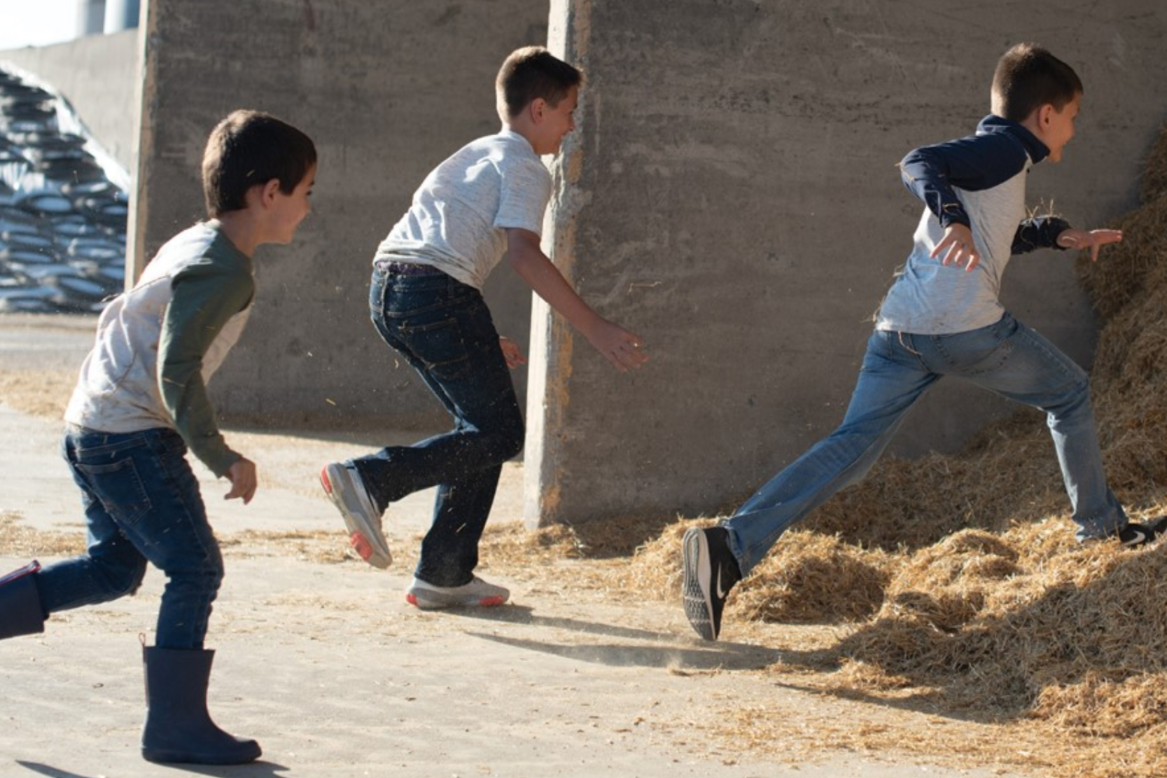 A group of young boys run toward a hay pile