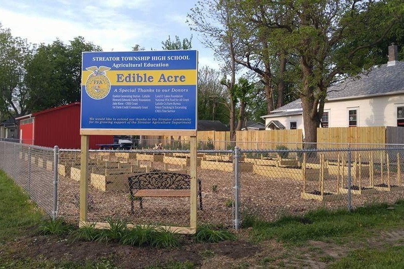 A blue sign that reads "Streator Township High School Agricultural Education Edible Acre."