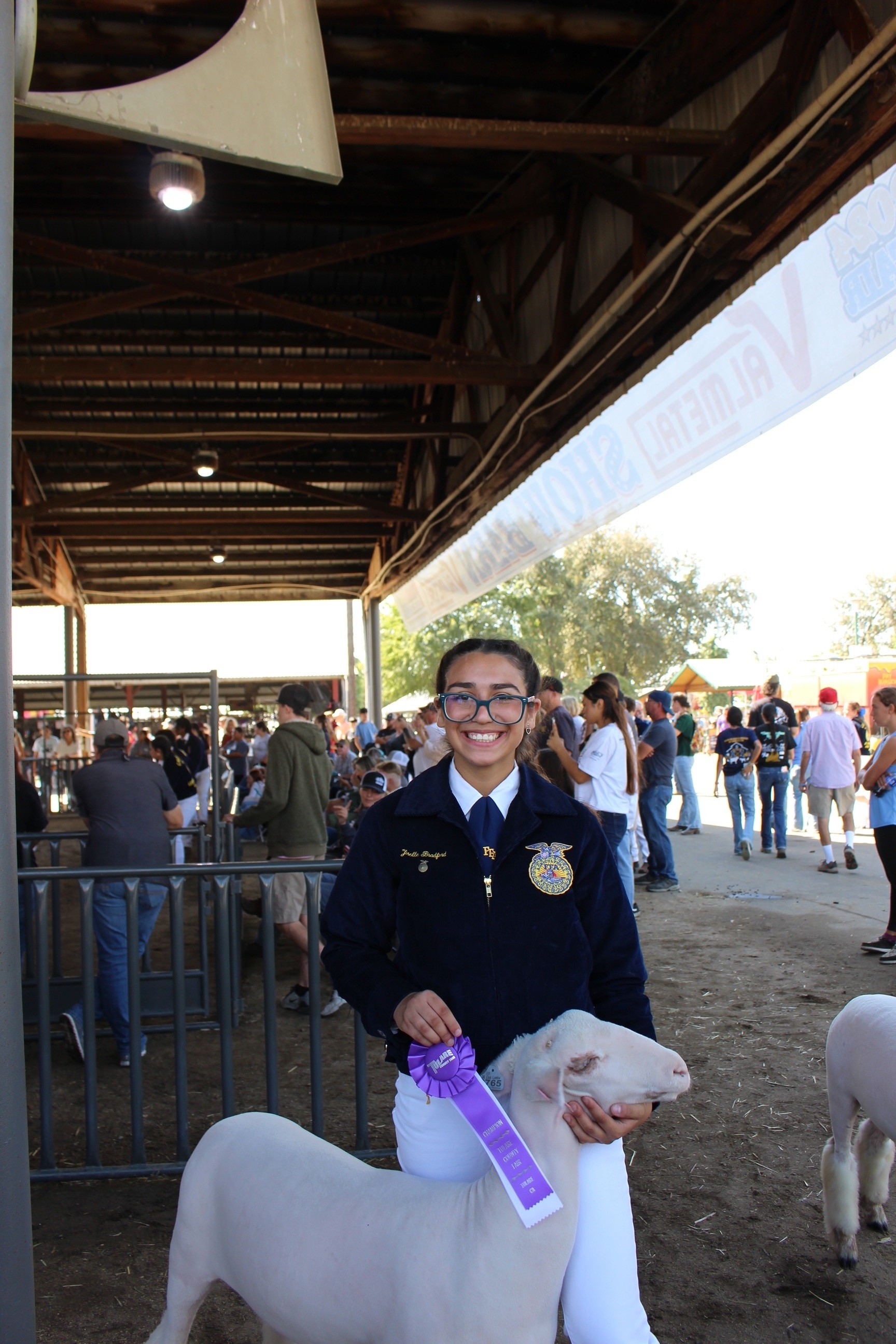 A young girl wearing an FFA jacket poses with a goat.