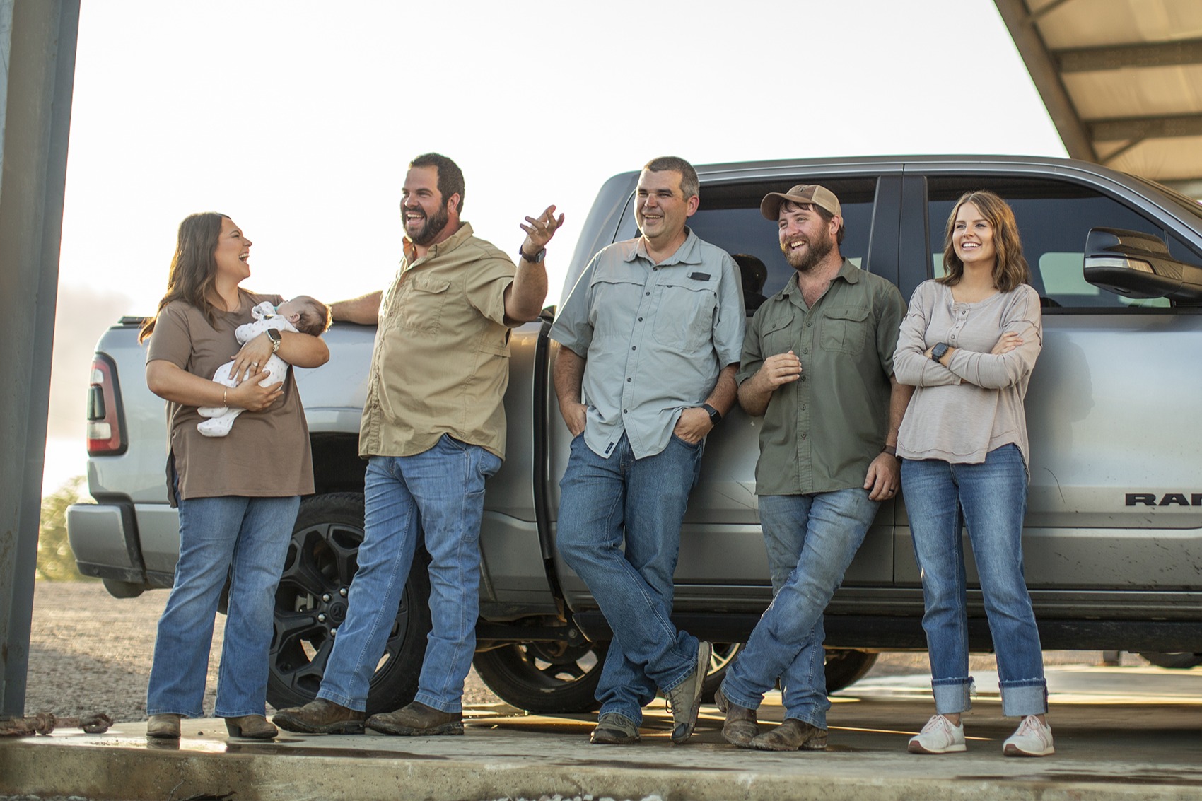 Five people and a baby standing and laughing near a pickup truck