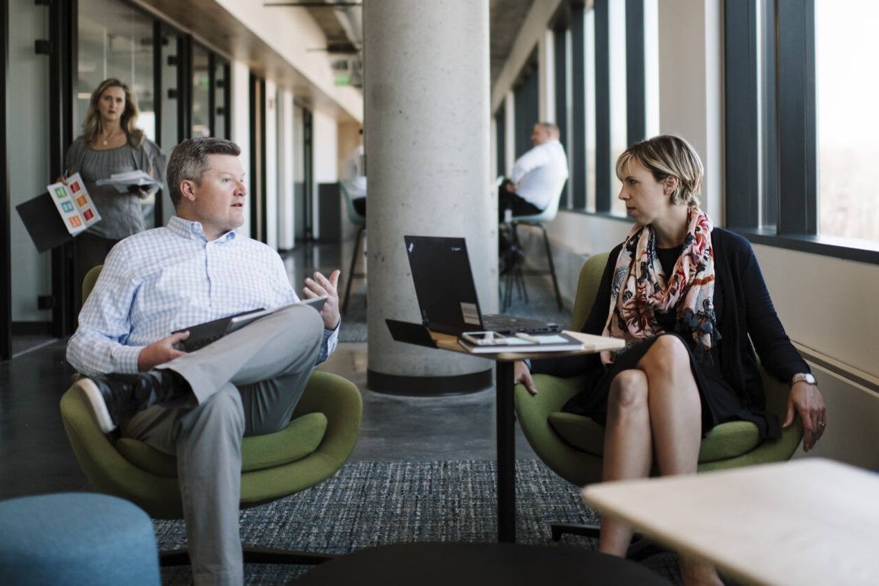 Two people sit across from each other and are discussing work.
