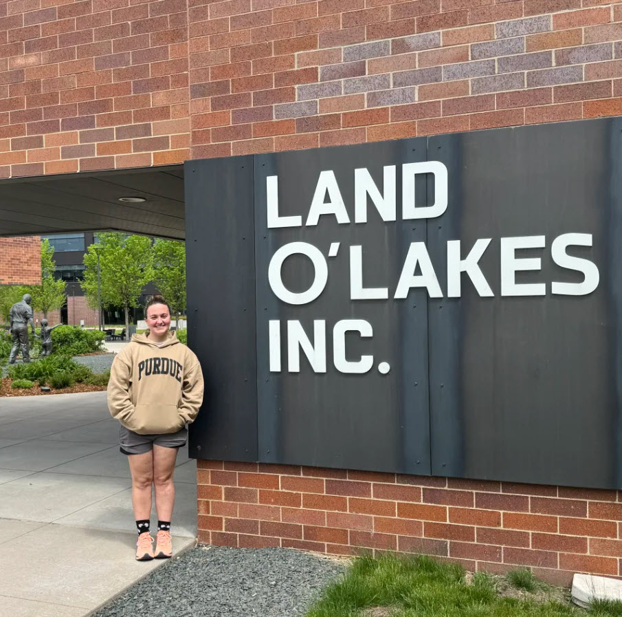 A woman in a Purdue sweatshirt poses next to a Land O'Lakes, Inc. sign.