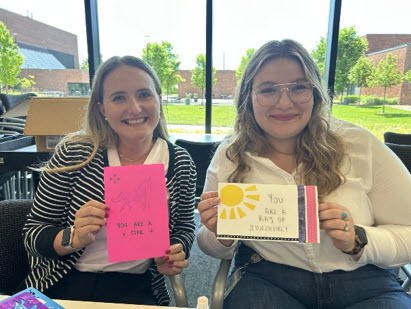 Two interns display handmade appreciation cards during a team activity in a meeting space.