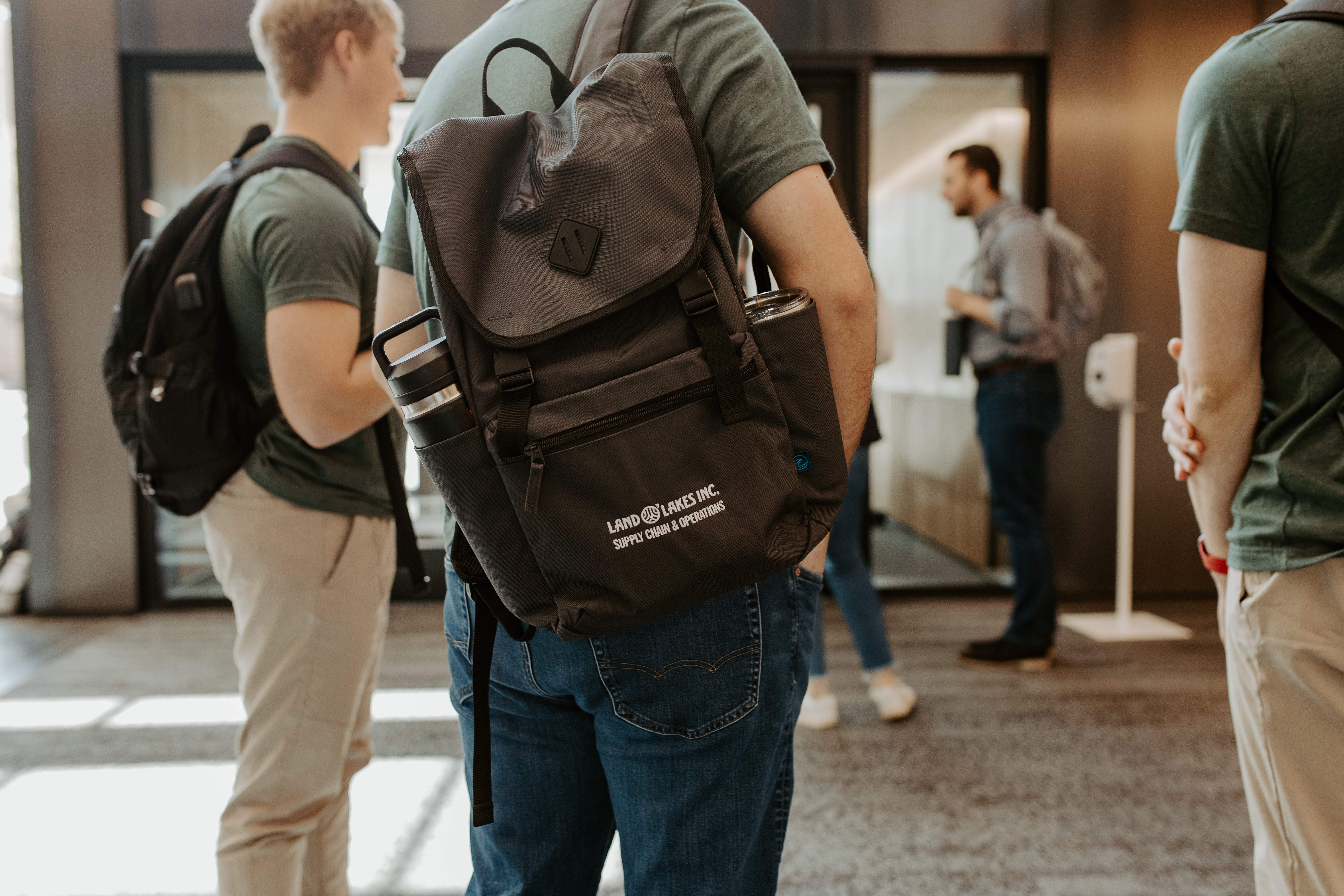 An intern stands in a crowd with a black Land O'Lakes Supply Chain backpack slung over his shoulder.