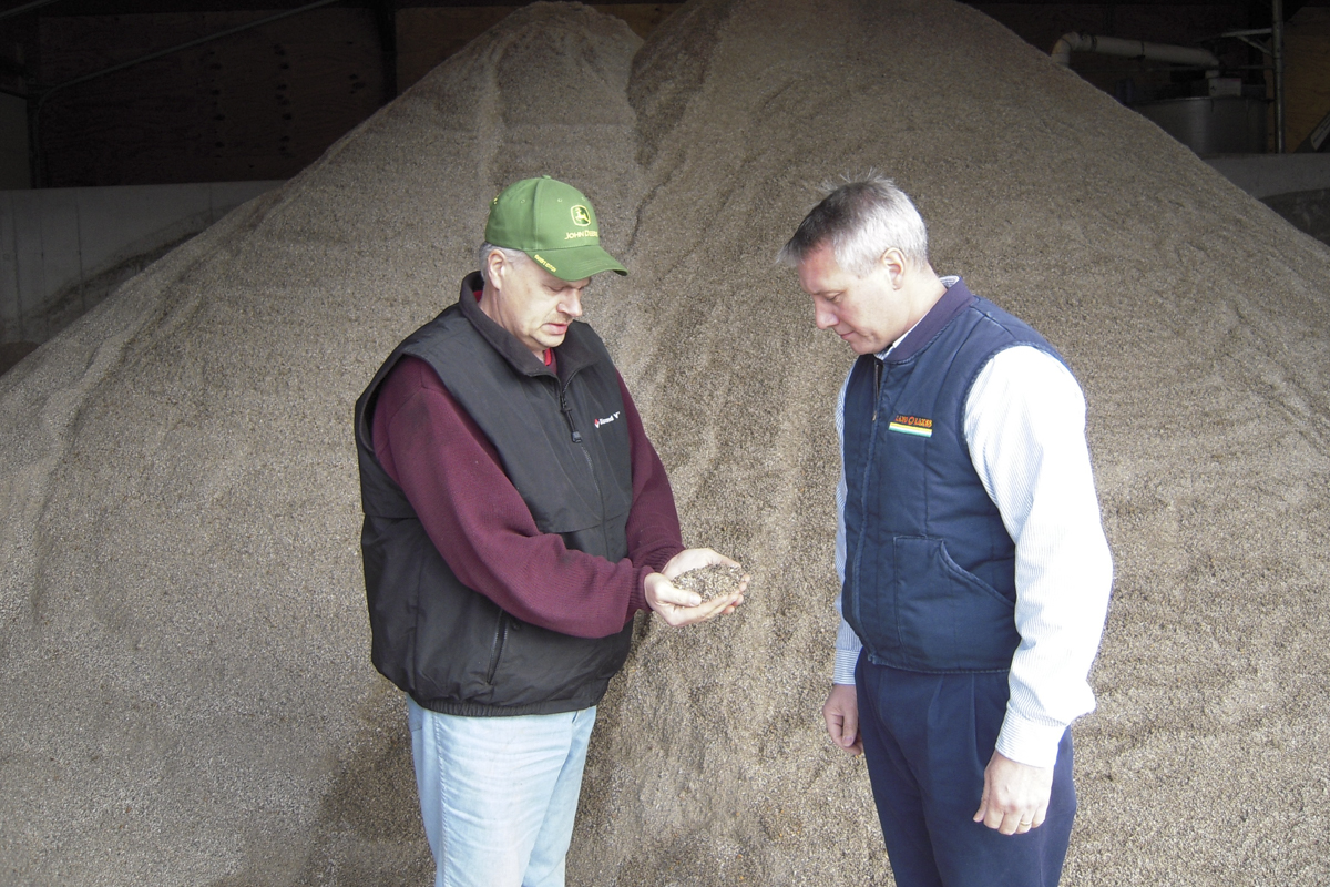 Two men stand in a grain bin observing grain.