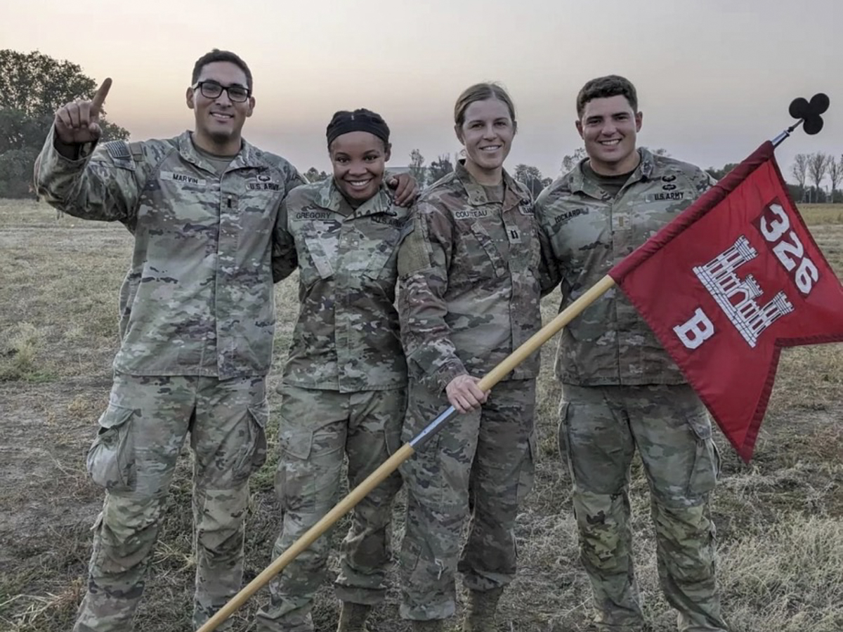 Four military members pose for a photo while holding a flag