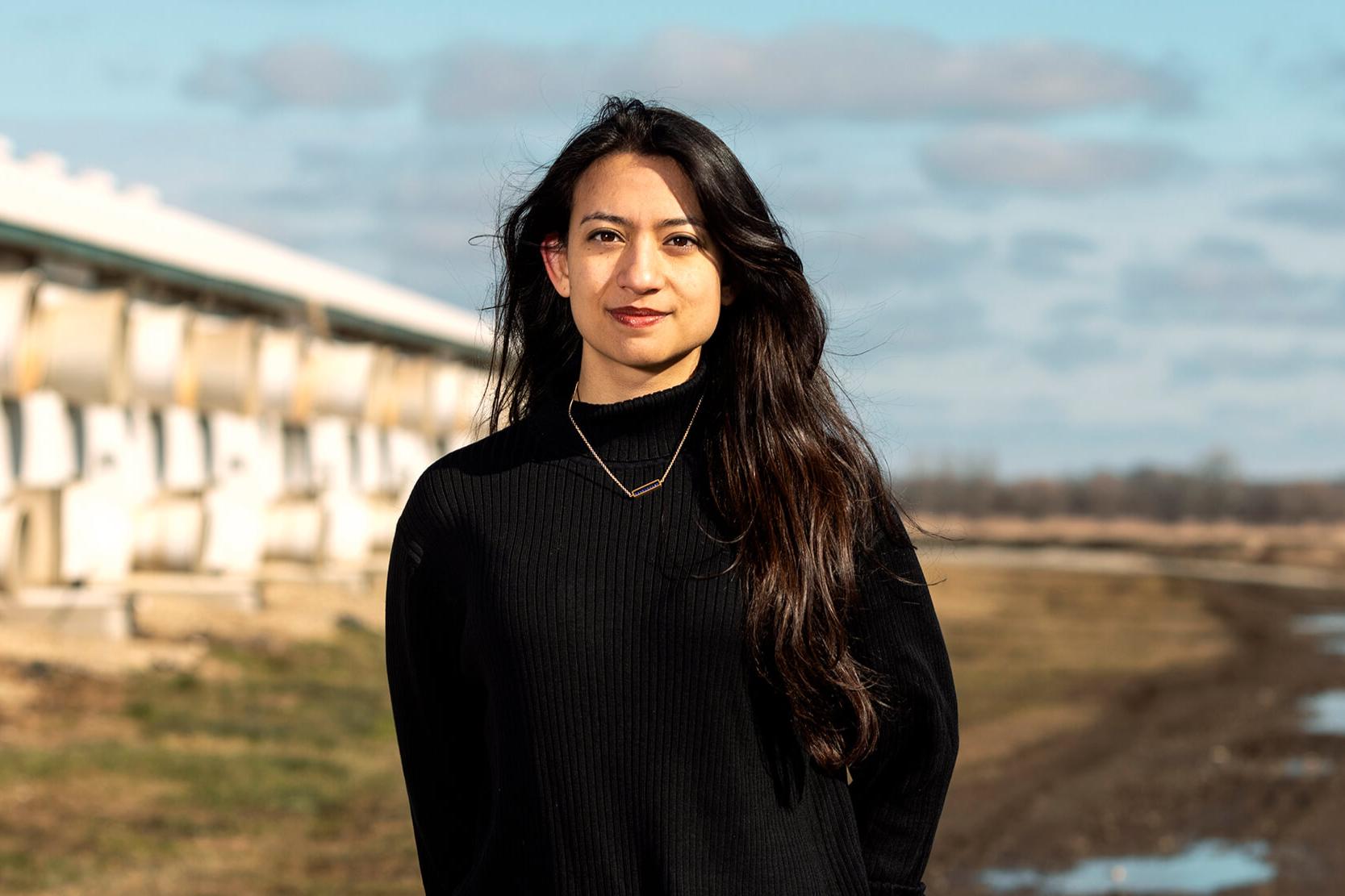 A woman with long dair hair wearing a black sweater standing in a field.